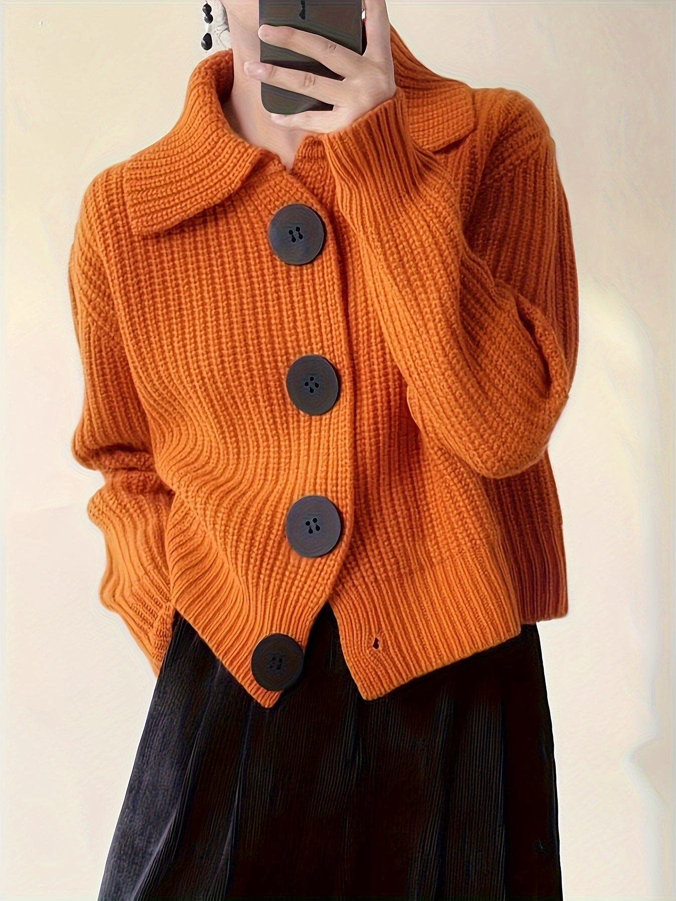 Orange knitted cardigan with black buttons worn by a person, against a neutral background